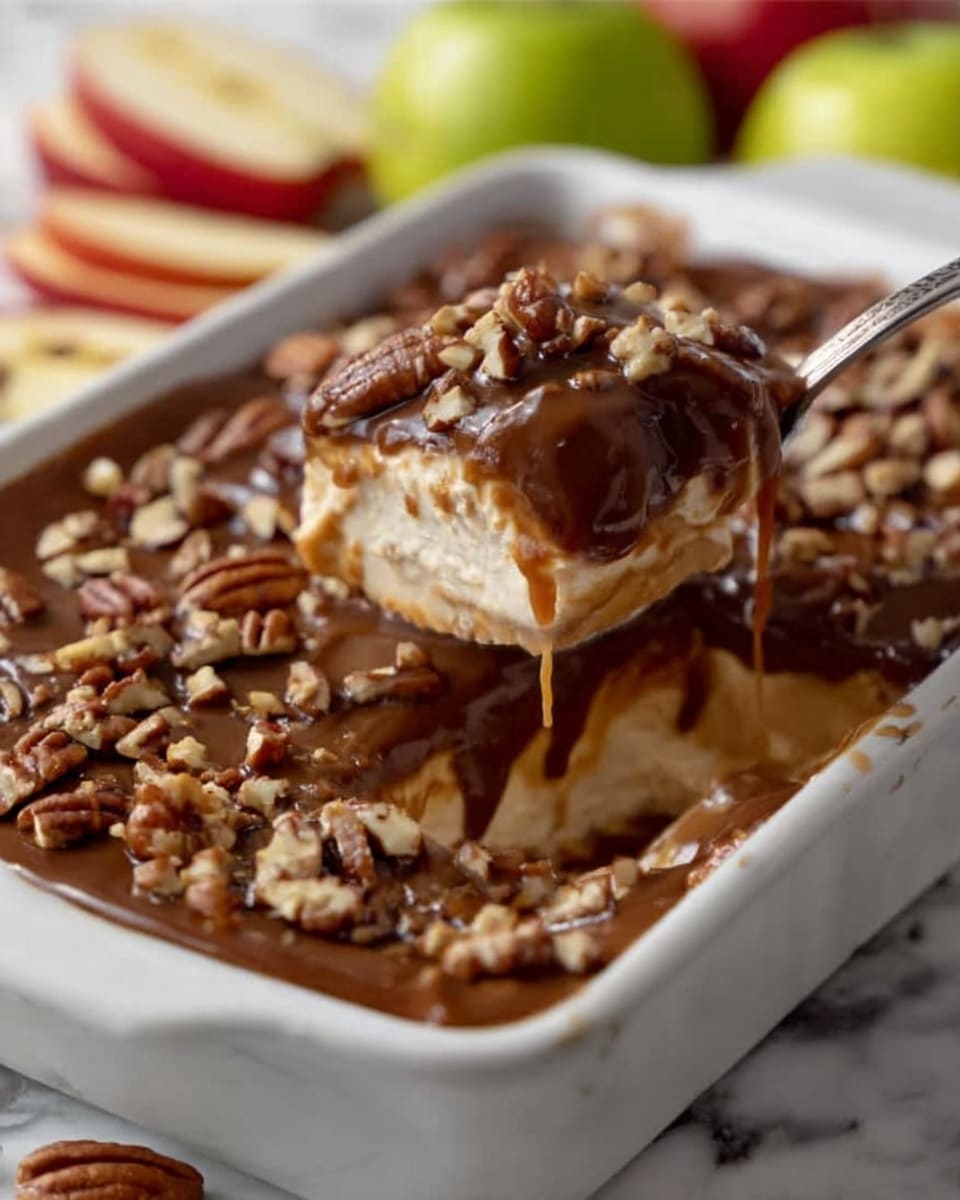 The image shows a white rectangular dish filled with a layered dessert. The bottom layer is creamy and light beige in color, topped with a thick layer of dark brown sauce that looks smooth and glossy. On top of the dark sauce, there are scattered small pieces of pecans adding a rough texture. A spoon digs into the dessert, lifting a scoop that reveals the creamy layer beneath the dark sauce. The dish is placed on a white marbled surface with green and red apple wedges visible in the background. Photo taken with an iphone --ar 4:5 --v 7