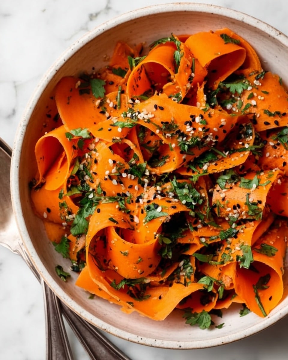 The image shows a white bowl filled with thin, wide orange carrot ribbons softly curled and layered within. The ribbons are sprinkled with small black and white sesame seeds and bright green chopped herbs, likely fresh cilantro, scattered evenly on top. The bowl sits on a white marbled surface and two silver salad serving forks lay nearby, slightly out of focus. The bright orange of the carrot ribbons contrasts with the green herbs and the speckled sesame seeds, creating a fresh and simple look. Photo taken with an iphone --ar 4:5 --v 7
