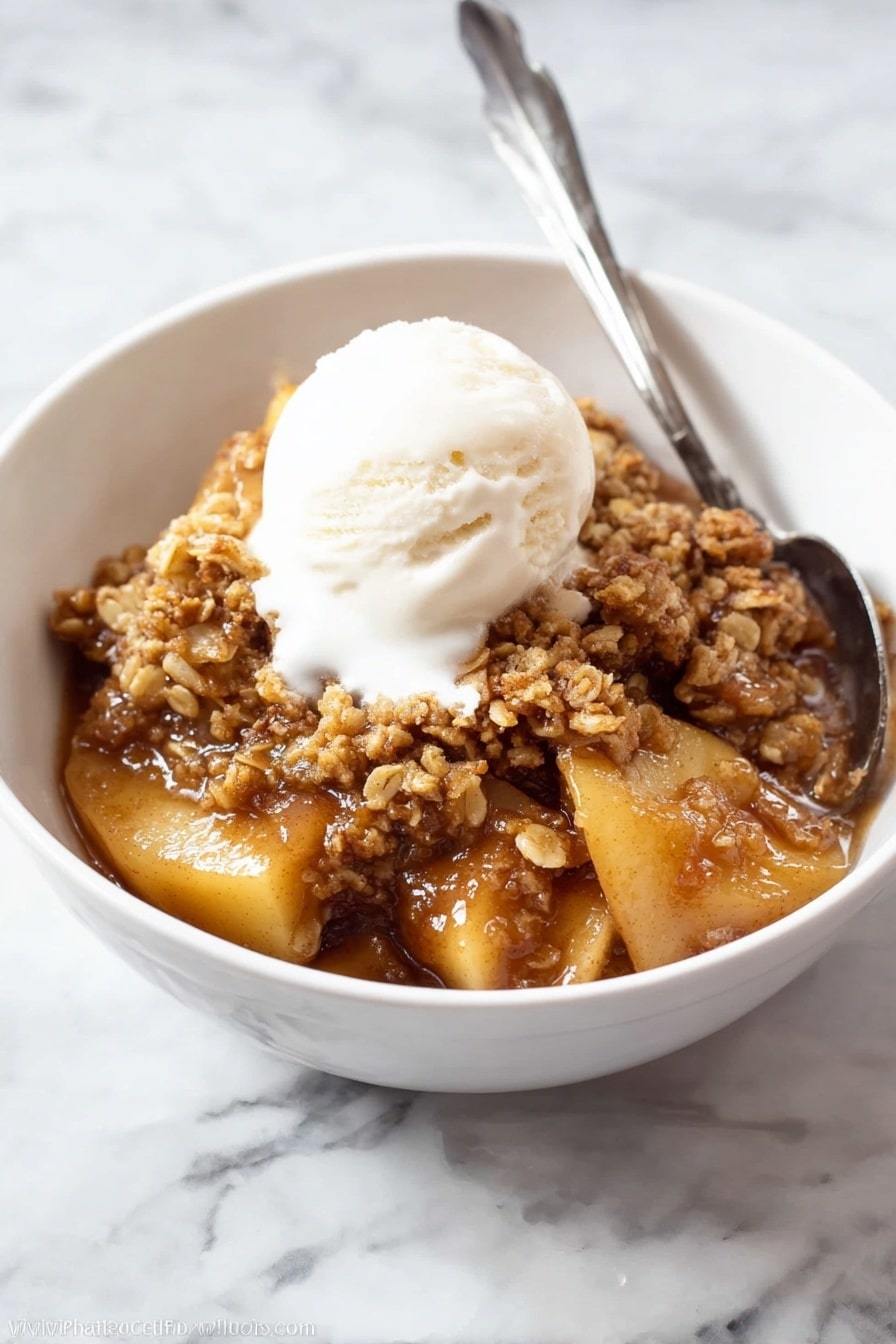 The image shows a white oval dish filled with a warm, brown dessert that has two main layers. The bottom layer is soft, cooked apple slices with a shiny, caramel-like sauce that looks sticky and rich. The top layer is a crumbly, golden brown oat and nut topping that covers the apples in uneven chunks. A silver spoon is dipped into the right side of the dish, slightly disturbing the topping and revealing more of the apple filling underneath. The dish is placed on a white marbled surface, making the warm colors of the dessert stand out. photo taken with an iphone --ar 2:3 --v 7 - The Best Apple Crisp, apple crisp dessert, easy apple crisp, homemade apple crisp, cozy apple crisp recipe