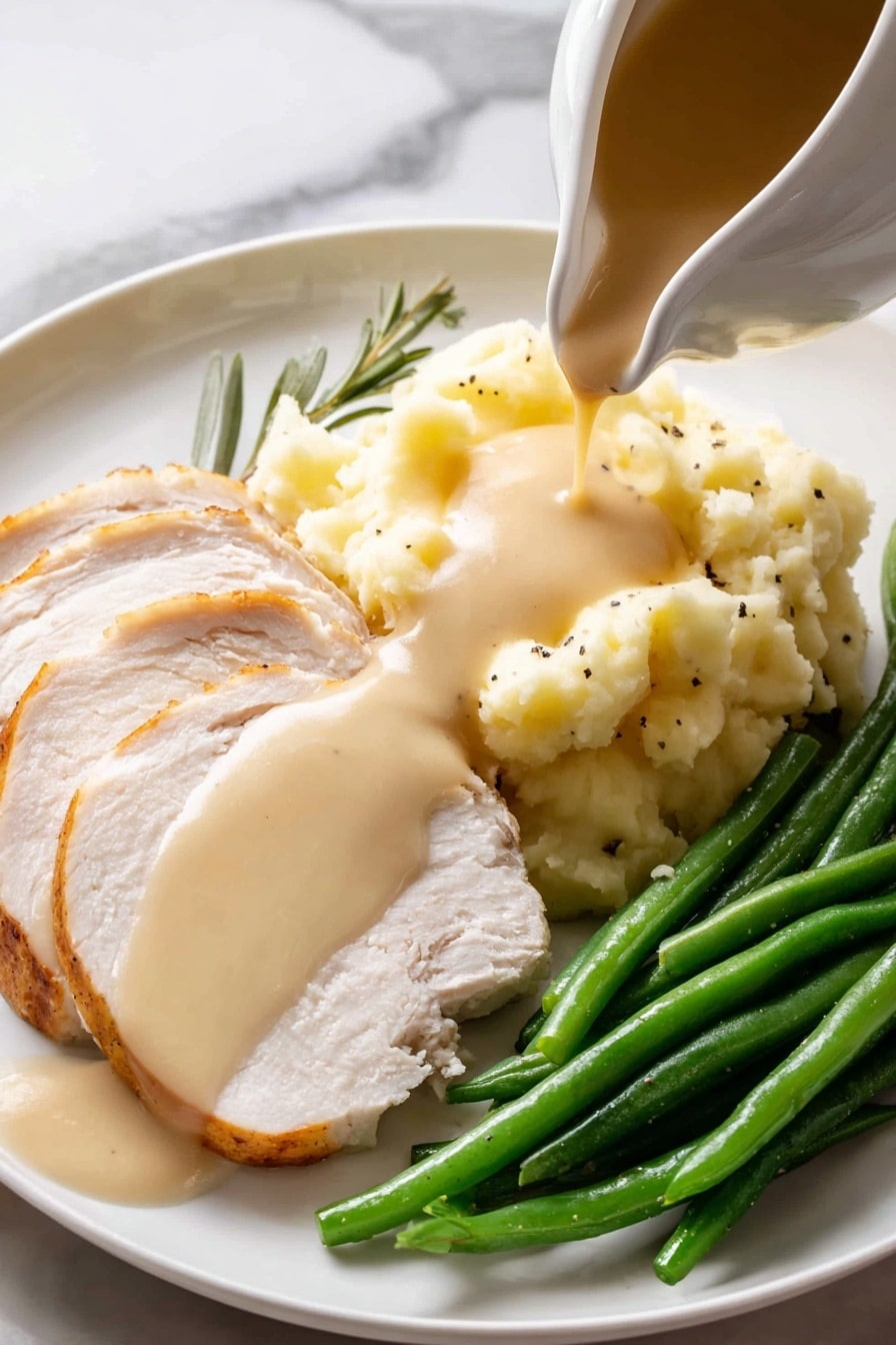A white gravy boat filled with light brown smooth sauce, speckled with black pepper, sits on a round white speckled plate with a brown rim. Two fresh green herb sprigs, one rosemary and one sage leaf, rest beside the gravy boat on the plate. A shiny silver spoon lies on the plate next to the gravy boat, and the entire setting is placed on a white marbled surface. photo taken with an iphone --ar 2:3 --v 7 - Easy Turkey Gravy From Drippings, turkey gravy recipe, homemade turkey gravy, simple holiday gravy, flavorful turkey gravy
