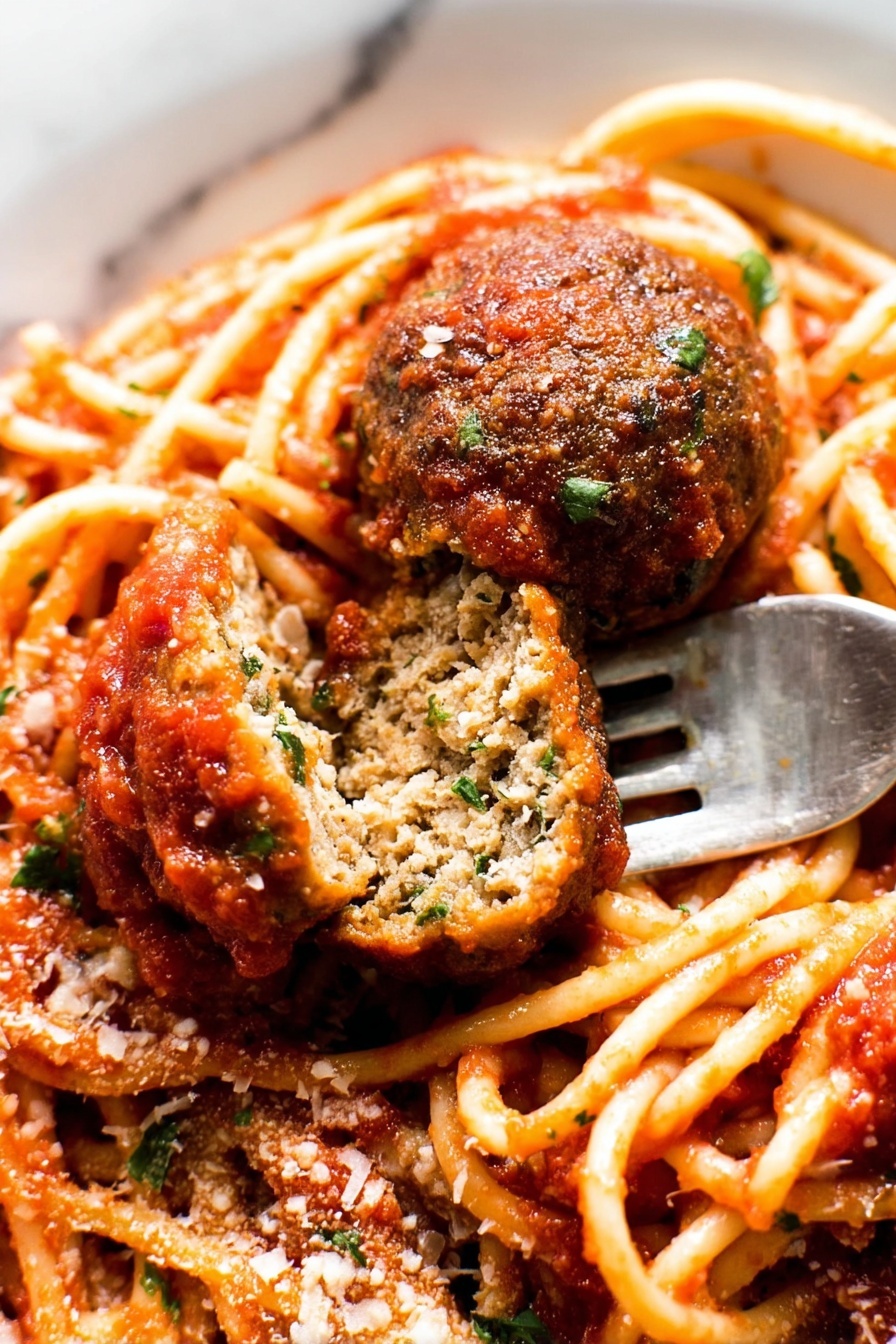 The image shows a close-up of a plate of spaghetti with tomato sauce and two meatballs, one whole and one cut in half to show its inside texture. The spaghetti is light orange with a smooth surface, coated with thick red tomato sauce that has small bits of herbs. The meatballs are brown with a slightly rough texture, and the cut meatball reveals a dense inside with green herbs mixed in. There is a sprinkling of grated cheese and chopped green herbs on top. A silver fork is placed under the cut meatball. The plate is white, and the background is a white marbled texture. photo taken with an iphone --ar 2:3 --v 7 - Classic Spaghetti and Meatballs, homemade spaghetti and meatballs, easy spaghetti recipe, Italian pasta dishes, comforting spaghetti dinner