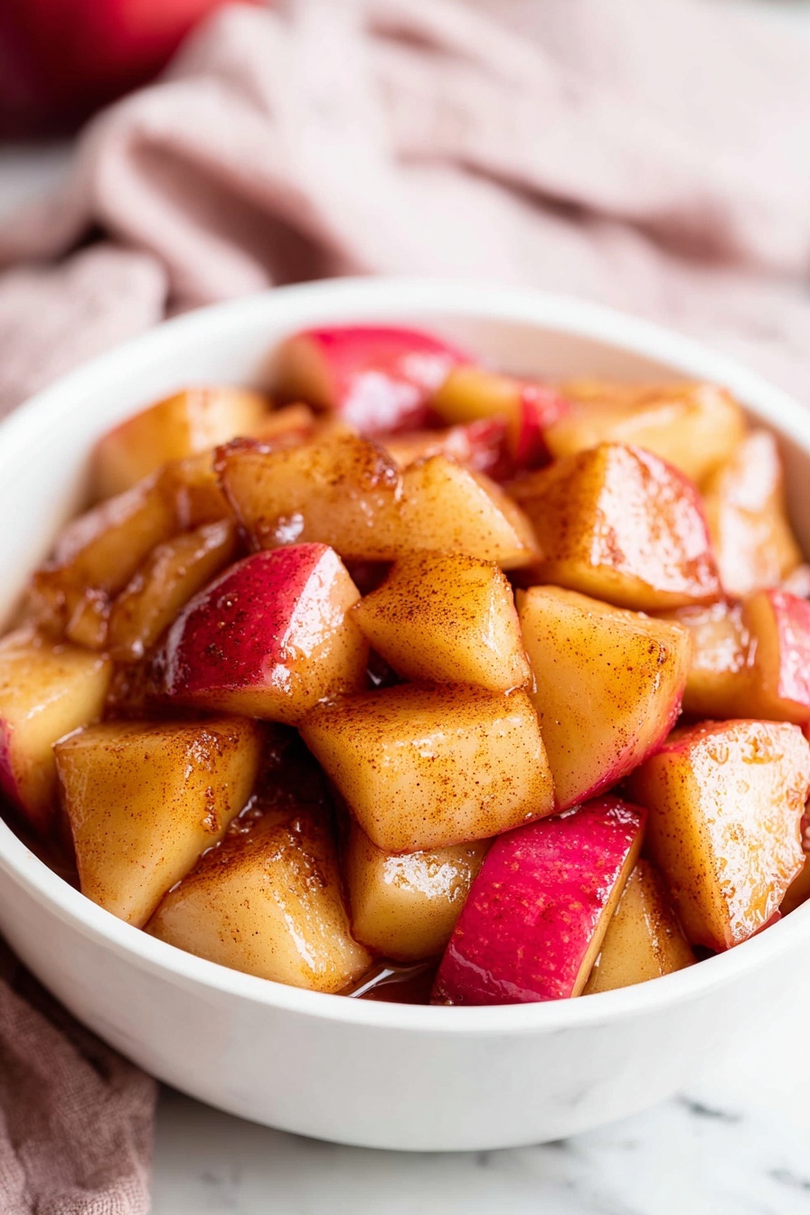 A black pan filled with evenly cooked, cubed apple pieces showing a mix of golden brown and red skin tones, lightly caramelized with a shiny texture scattered all over the pan; the pan handle is metal with visible wear and sits on a white marbled surface partially covered by a soft red and white checkered cloth. To the top right, two whole red apples rest on a small round wooden board. The image is bright and simple, focusing on the warm colors and textures of the cooked apples. photo taken with an iphone --ar 2:3 --v 7 - Easy Cinnamon Apples, cinnamon apple dessert, quick apple snack, healthy apple side dish, cozy apple recipes