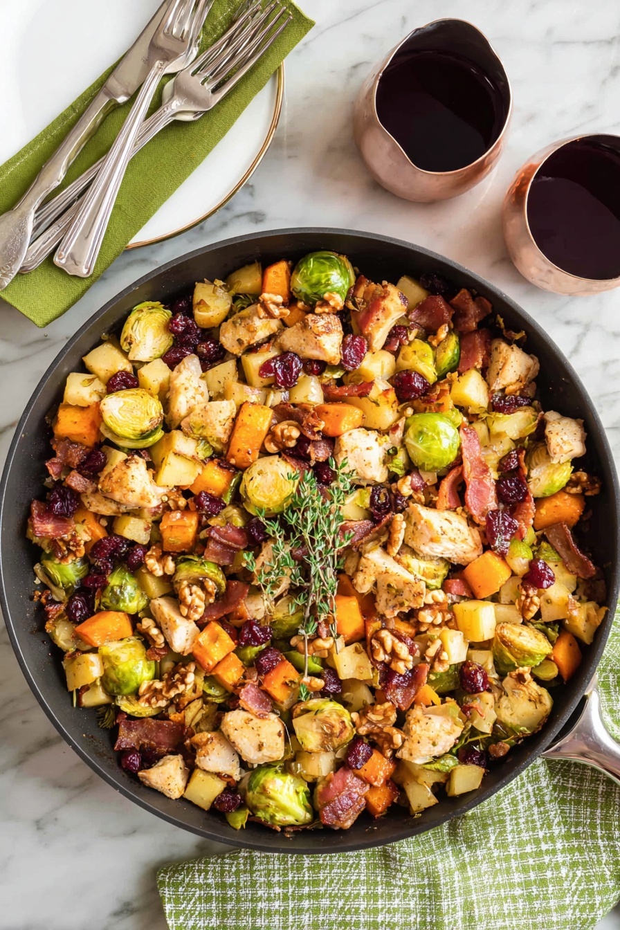 A large black pan filled with a colorful mix of cooked ingredients sits on a white marbled surface with a green cloth and fork on the left. The mix has three main layers: a base of cubed orange sweet potatoes, light yellow apple pieces, and halved green Brussels sprouts; a middle layer of beige chicken pieces and crispy, dark brown bacon bits; and a top layer of whole walnuts and dried dark red cranberries. A small sprig of fresh green thyme rests on top, and a wooden spoon leans inside the pan from the right side. Two glasses filled with dark red wine are placed nearby on the white marbled surface, with one glass partially reflected on a shiny black bowl. photo taken with an iphone --ar 2:3 --v 7 - One-Pot Easy Harvest Chicken Skillet, fall chicken skillet, cozy weeknight dinner, healthy chicken and vegetable skillet, simple one-pan chicken meal
