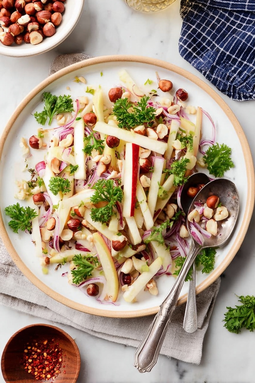 The image shows a white plate filled with a fresh salad consisting of thin, pale yellow sticks of apple with red skin edges, thin slices of purple-red onion bent softly, and scattered small whole brown hazelnuts along with some halved ones. Bright green parsley leaves are sprinkled on top, adding color contrast. A silver spoon and fork rest on the right side of the plate, partly on the salad. The plate is set on a white marbled surface. photo taken with an iphone --ar 2:3 --v 7 - Kohlrabi Slaw with Apples and Hazelnuts, healthy kohlrabi slaw, crunchy fruit and nut salad, fresh vegetable slaw recipes, easy side salads