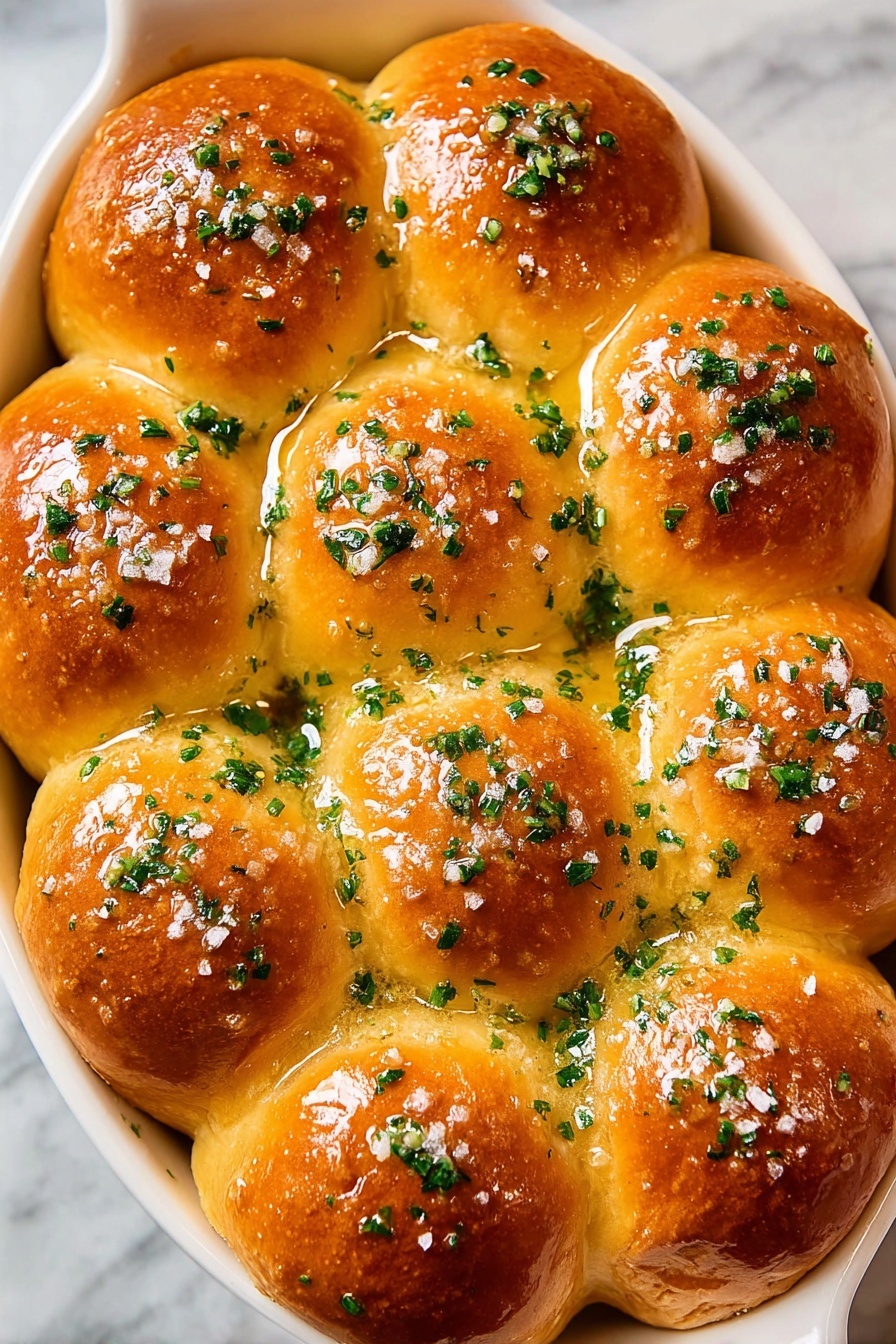The image shows a white oval dish filled with 15 golden brown rolls arranged in a close cluster. Each roll has a smooth, shiny surface that looks soft and fluffy with a slight crisp on top. The rolls are topped with chopped green herbs spread evenly, adding fresh color contrast. There is a light glaze that makes the rolls appear moist, and small bits of coarse salt can be seen scattered on the surface. The dish is set on a white marbled texture background. photo taken with an iphone --ar 2:3 --v 7 - Garlic Butter Dinner Rolls, fluffy dinner rolls with garlic butter, homemade garlic bread rolls, soft bread rolls recipe, easy garlic dinner rolls