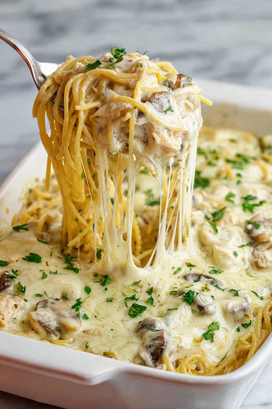 A white baking dish filled with creamy baked spaghetti is shown, featuring one thick layer of pasta mixed with mushrooms and shredded chicken, all covered with a smooth, melted white cheese sauce. The top layer is sprinkled with chopped fresh green herbs. A silver serving spoon lifts a portion of the spaghetti noodles, showing the soft texture and strands of melted cheese stretching from the dish. The background has a white marbled texture. Photo taken with an iphone --ar 2:3 --v 7 - Easy Chicken Tetrazzini Casserole, chicken tetrazzini casserole, creamy chicken pasta bake, cheesy chicken casserole, comforting chicken pasta dish