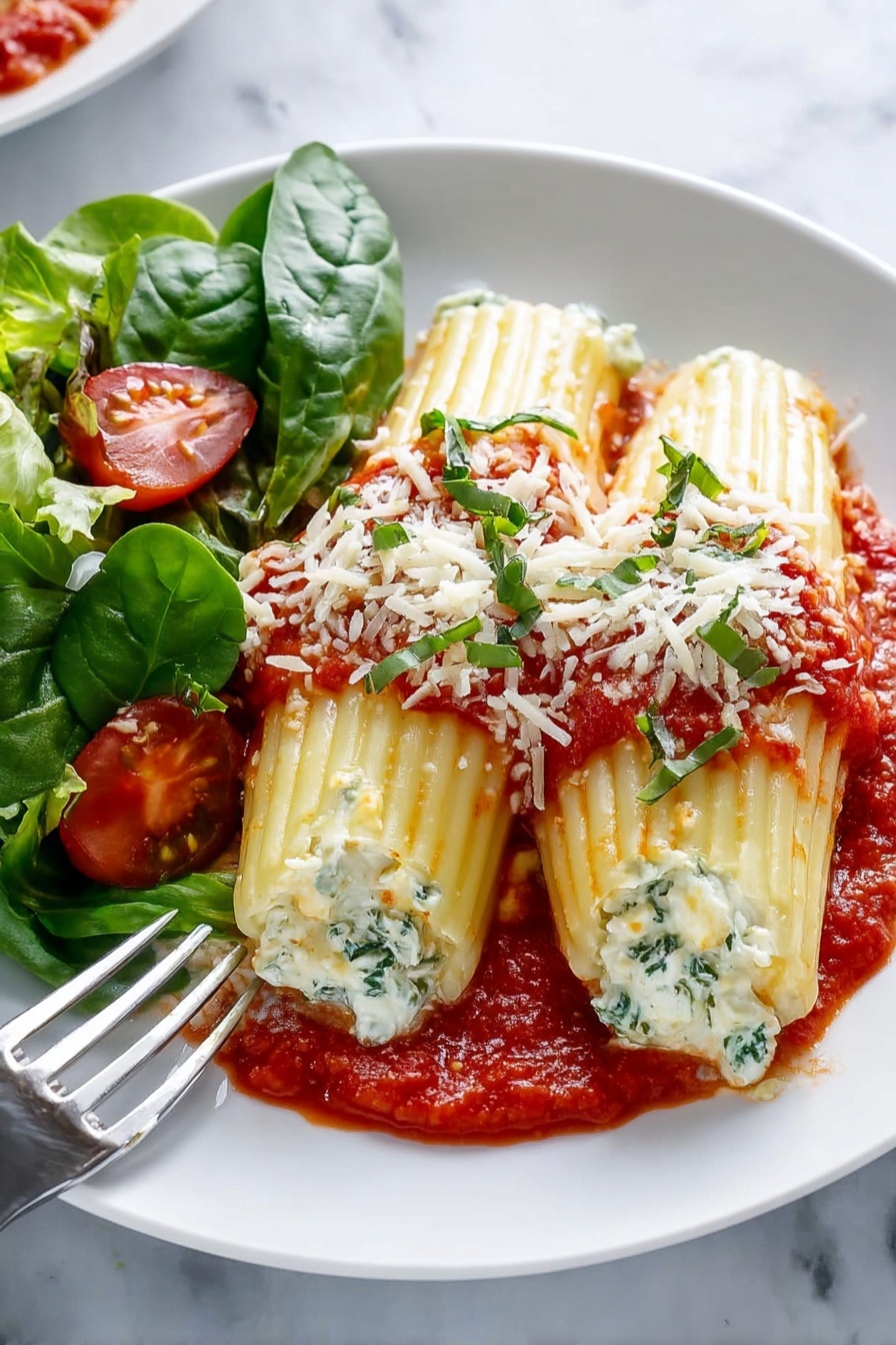 A white baking dish filled with seven folded pasta shells arranged in two rows. Each shell is stuffed with a white creamy filling and topped with bright red tomato sauce that is chunky and spread in small piles along the top. Fresh green basil leaves and small bits of grated white cheese are scattered on top, adding color contrast. The thick red sauce lines the bottom and sides of the dish, and the pasta shells have a ridged texture and a soft yellow color. The dish sits on a white marbled surface. Photo taken with an iphone --ar 2:3 --v 7 - Cheese Manicotti, Italian cheese manicotti, baked cheese manicotti, creamy cheese stuffed pasta, easy cheese manicotti