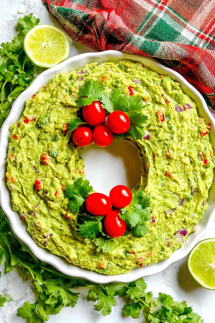 A white round dish with a thick single layer of chunky green guacamole spread evenly in a ring shape, leaving a clear circular space in the center. The guacamole is mixed with bits of red, purple, and green from chopped vegetables. On top of the guacamole, there are three small clusters of three bright red cherry tomatoes each, paired with a few green cilantro leaves around them. The dish sits on a white marbled surface with a red, green, and beige plaid cloth draped softly around the top edge. Beside the dish are fresh cilantro sprigs and two lime halves, one whole and one sliced. photo taken with an iphone --ar 2:3 --v 7 - Christmas Guacamole Wreath, festive guacamole appetizer, holiday party dips, Christmas appetizer ideas, easy holiday party recipes