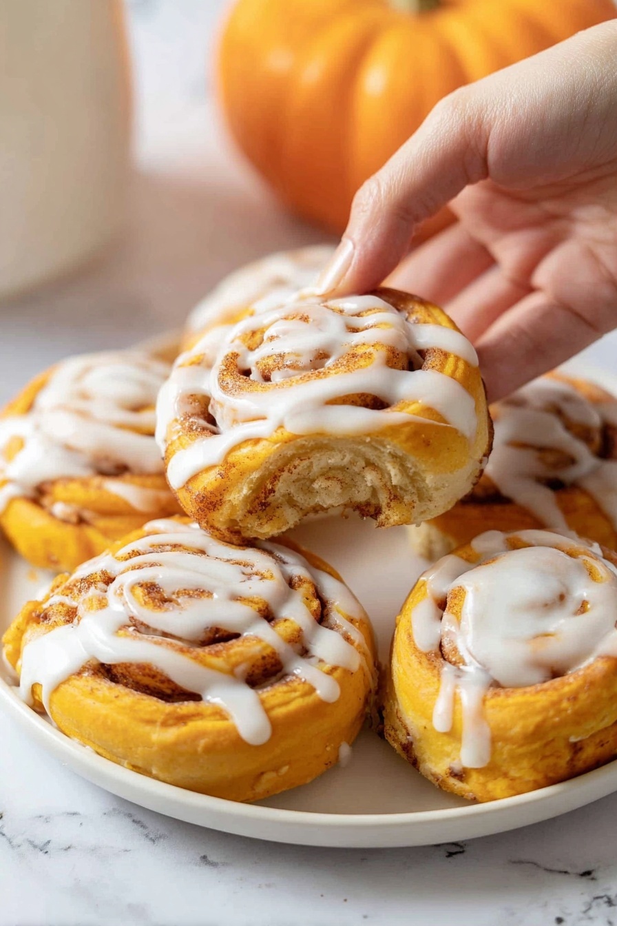 A white plate filled with six bright orange spiral rolls, each topped with a thick drizzle of white icing. The rolls have multiple visible layers with a soft, doughy texture and a cinnamon-spice swirl inside that adds a speckled light brown pattern. A woman's hand is gently lifting one roll from the plate, showing more of its smooth icing on the top center. The background is a white marbled texture with a small orange pumpkin blurred in the back. photo taken with an iphone --ar 2:3 --v 7 - Pumpkin Cinnamon Rolls with Cream Cheese Glaze, fall cinnamon roll recipes, easy pumpkin cinnamon rolls, homemade pumpkin cinnamon rolls, cozy fall breakfast recipes