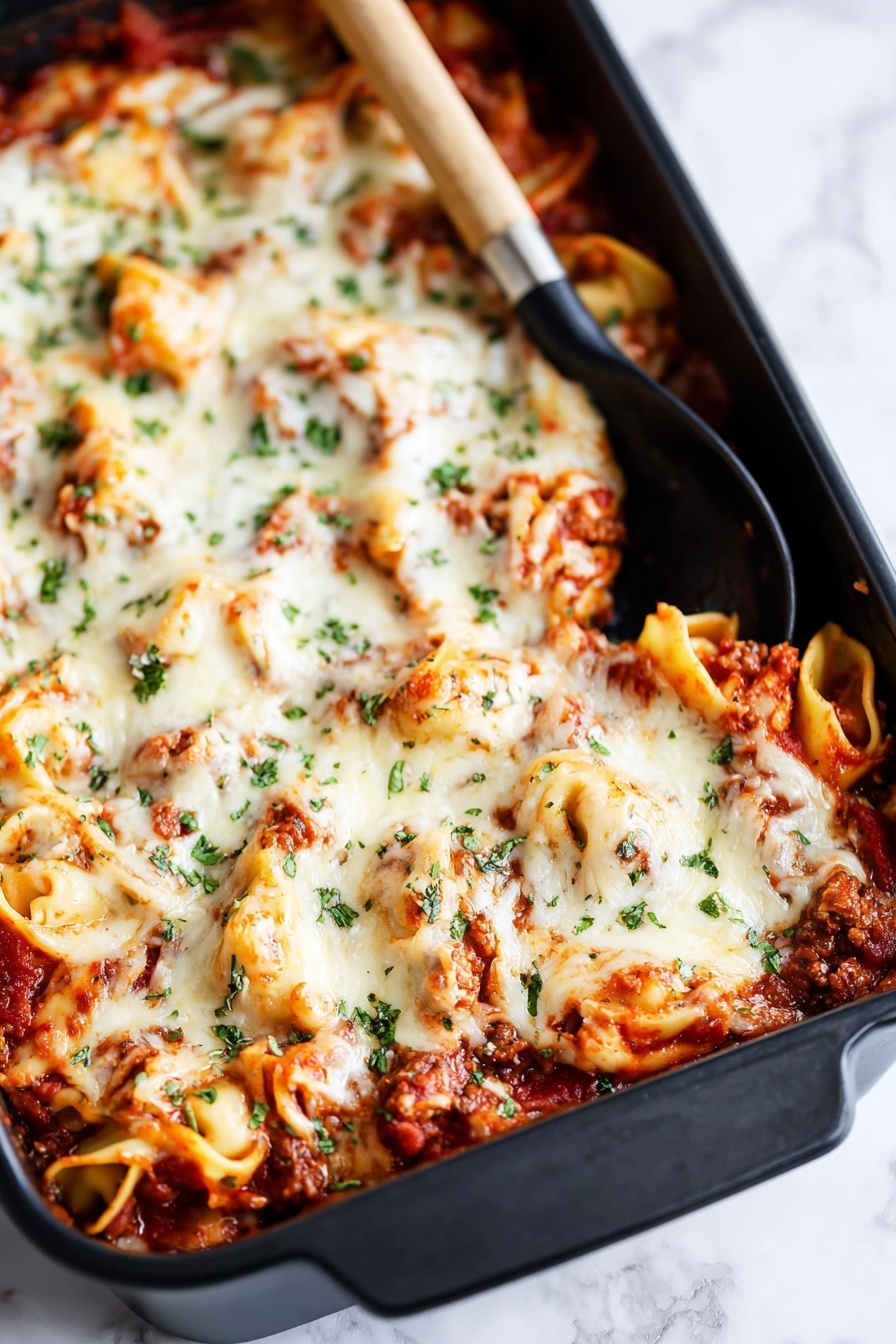 The image shows a large black baking dish filled with a layered pasta bake. The bottom layer has visible tomato sauce with small chunks of meat, rich red in color. On top of this is a thick layer of melted white cheese, which looks creamy and slightly browned in some spots. Scattered green herbs, probably parsley or basil, are sprinkled over the cheese, adding color contrast. There are curled pasta pieces, possibly tortellini, peeking through the cheese layer, coated in sauce and cheese. A black spoon with a wooden handle rests inside the dish near the top corner. The dish is placed on a white marbled surface. Photo taken with an iphone --ar 2:3 --v 7 - Baked Tortellini with Cheese, cheesy tortellini casserole, easy baked tortellini recipe, hearty cheese tortellini bake, family-friendly pasta casserole