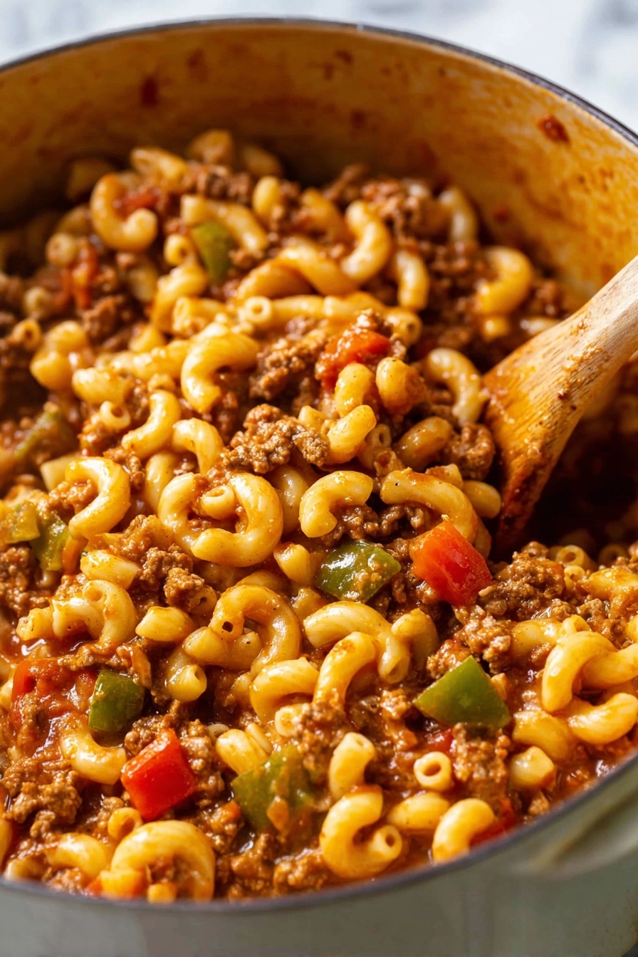 The image shows a close-up of a pot filled with elbow macaroni pasta mixed with ground meat, diced tomatoes, and chopped green bell peppers. The pasta is soft and coated with a rich reddish-brown sauce. The ground meat is crumbled small and evenly spread throughout the dish. Bright red tomato pieces and small chunks of green bell peppers add pops of color. A wooden spoon is stirring the mixture on the right side. The pot has a soft brown inside texture, and the background is a white marbled surface. photo taken with an iphone --ar 2:3 --v 7 - American Chop Suey, American Chop Suey recipe, comforting dinner ideas, easy weeknight meal, hearty pasta dish