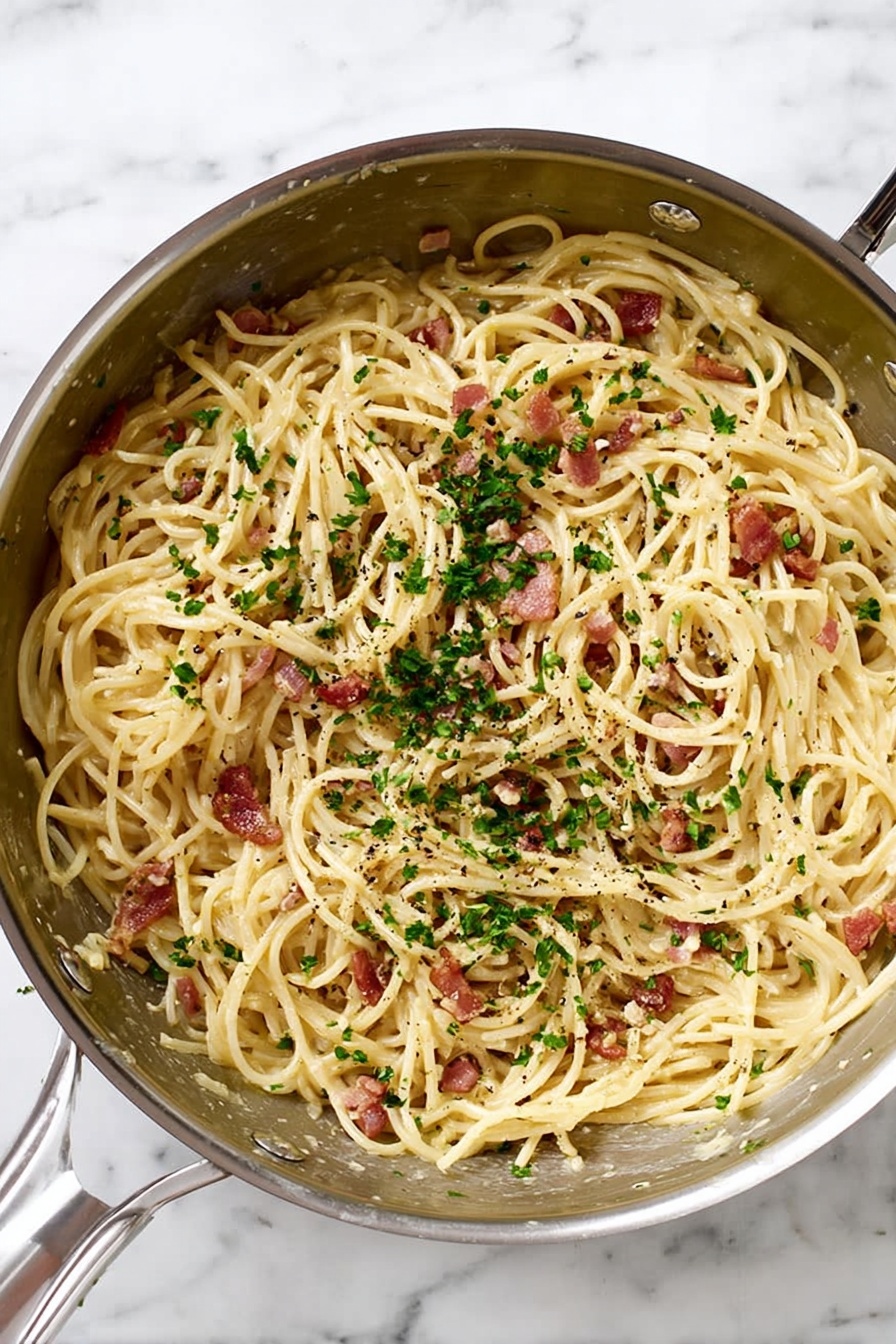 A silver metal pan filled with spaghetti noodles mixed with small pieces of reddish-brown bacon and finely chopped green parsley sprinkled on top. The pasta has a light cream sauce coating, and tiny black pepper bits are scattered throughout. The pan is placed on a white marbled surface. Photo taken with an iphone --ar 2:3 --v 7 - Spaghetti Carbonara with Bacon, Easy Spaghetti Carbonara, Quick Italian Pasta, Creamy Bacon Pasta, Classic Spaghetti Carbonara