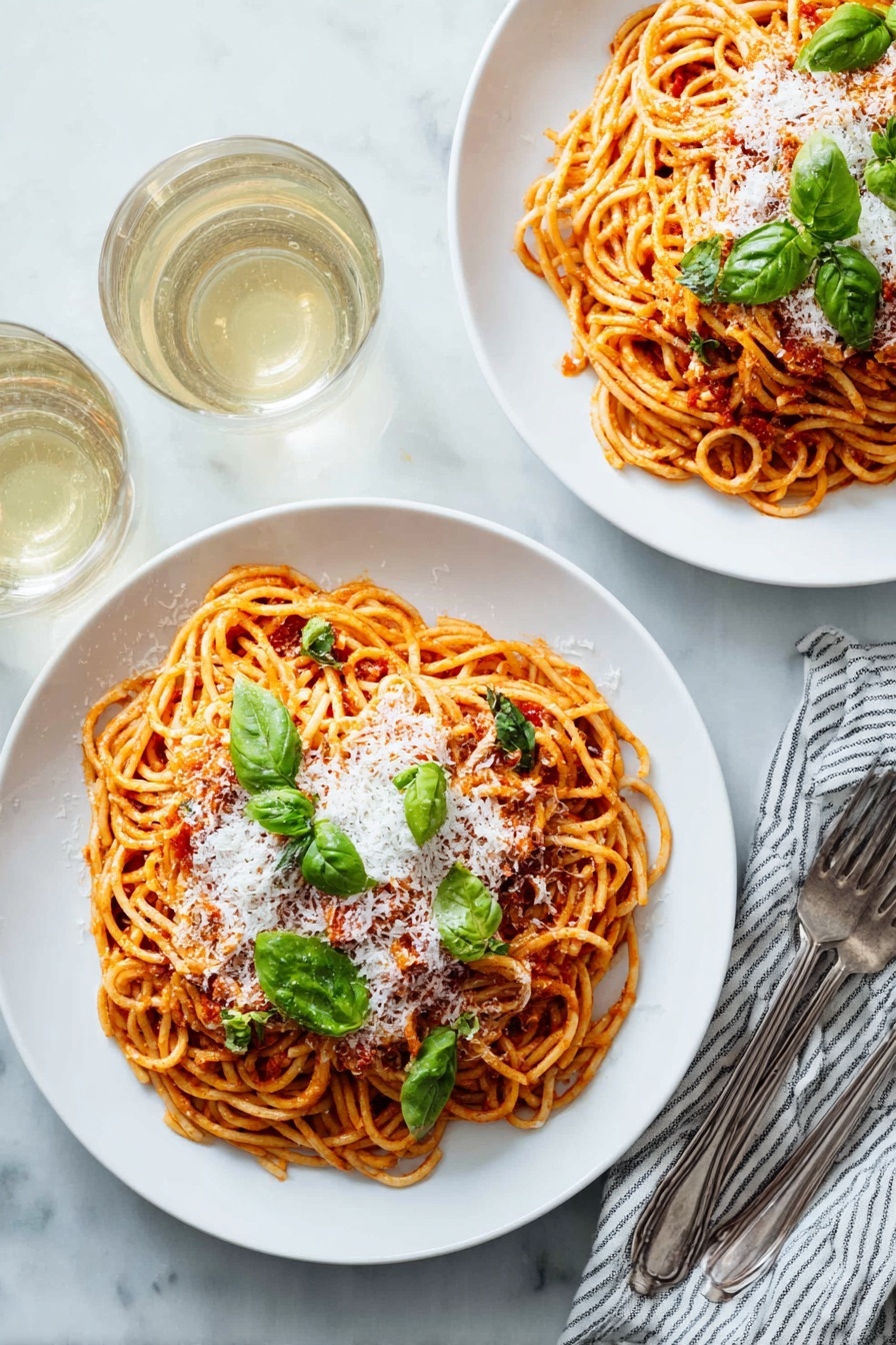 Two white plates with round shapes, each holding a serving of spaghetti layered with red tomato sauce, topped with a layer of white grated cheese and scattered green basil leaves. The spaghetti is twisted into small nests that fill most of the plate. Near the plates are two forks resting on a white and blue striped cloth napkin, and two almost full glasses of white wine are seen in the top left corner. Everything is set on a white marbled table surface. photo taken with an iphone --ar 2:3 --v 7 - Simple Pasta Pomodoro with Fresh Basil, easy Italian pasta recipe, quick tomato basil pasta, authentic pasta pomodoro, fresh basil pasta dish