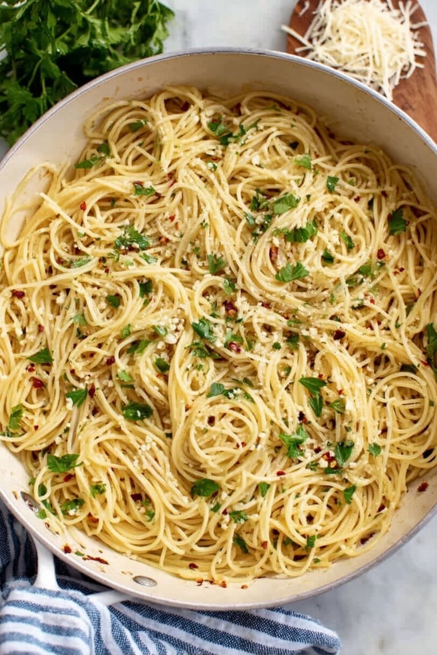 A white pan filled with a single layer of thin spaghetti pasta cooked and mixed with small bits of white garlic and red chili flakes spread throughout. Fresh green parsley leaves are scattered on top, adding a touch of color and freshness. The pan rests on a white marbled surface next to a blue and white striped cloth, with fresh parsley and some shredded cheese partially visible in the background. Photo taken with an iphone --ar 2:3 --v 7 - Garlic Oil Spaghetti, garlic pasta recipe, quick Italian pasta, easy garlic spaghetti, flavorful garlic pasta