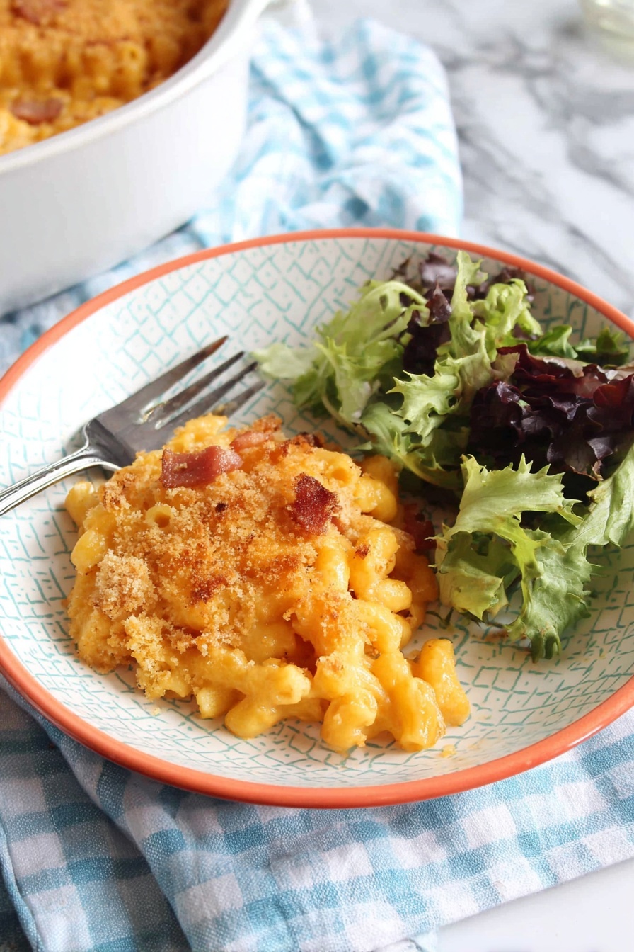 A white bowl with a light geometric pattern and orange rim holds a serving of baked macaroni and cheese topped with a golden breadcrumb crust with some browned spots. The macaroni pasta under the crust is creamy and orange, with small pieces of browned bacon or ham mixed inside. To the right side of the bowl is a small fresh salad of mixed green leaves, some dark purple and others bright green with curly texture. A silver fork rests on the left edge of the bowl. The bowl sits on a blue and white checkered cloth over a white marbled surface. In the bottom left corner, part of a white round baking dish filled with more macaroni and cheese is visible. photo taken with an iphone --ar 2:3 --v 7 - Chorizo Mac and Cheese Bake, spicy cheesy pasta, smoky chorizo casserole, easy ham and cheese bake, hearty comfort food