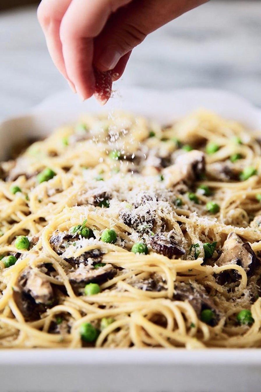 A round serving of baked pasta with visible noodles, small green peas, and bits of light beige chicken arranged in the center of a shiny white plate with a blue rim. The top layer is sprinkled with golden toasted breadcrumbs, adding a rough texture. A silver fork is placed on the right side of the plate, its tines partly under the pasta. The plate rests on a white marbled surface, and in the blurry background, there is a white baking dish filled with more of the same pasta bake. The light is soft and natural, showing the creamy and slightly browned surface of the pasta. photo taken with an iphone --ar 2:3 --v 7 - Turkey Mushroom Pasta Bake, easy comfort pasta bake, hearty turkey pasta dish, cheesy mushroom pasta casserole, quick baked pasta with turkey