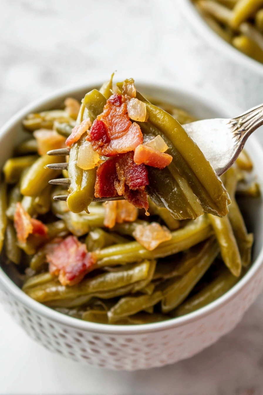 A white bowl with a pattern holds cooked green beans layered at the bottom, soft and shiny with a slightly wrinkled texture. On top, small chunky pieces of browned bacon with a reddish-brown tone and a bit of translucent cooked onion are mixed in. A fork lifts some green beans and bacon from the bowl, showing the layers clearly, with the vegetables still moist and the bacon crispy in places. The background is a white marbled surface. photo taken with an iphone --ar 2:3 --v 7 - Crock Pot Green Beans with Bacon, easy green beans with bacon, slow cooker green beans, savory green bean side dish, bacon green beans recipe