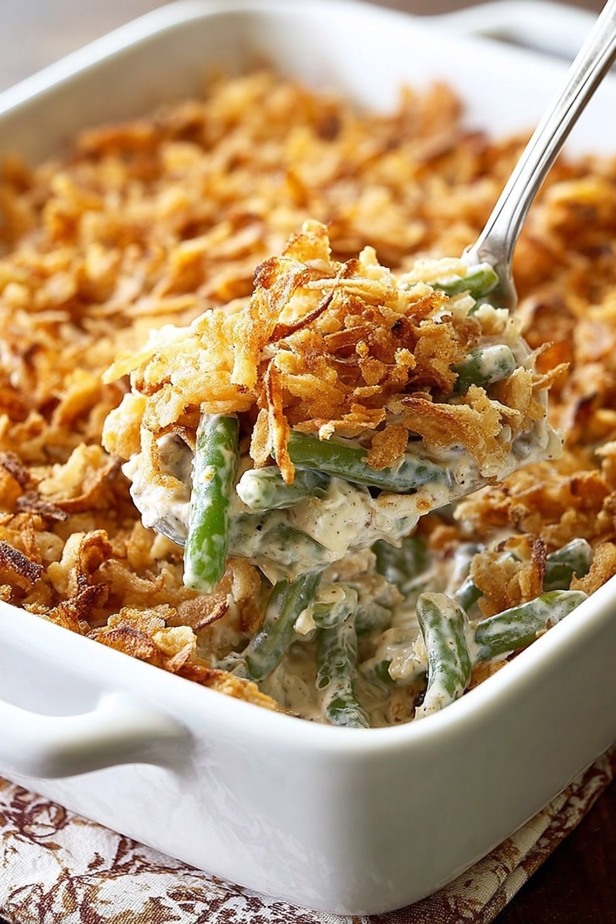 A white rectangular baking dish filled with a creamy green bean casserole topped with a thick layer of crispy golden brown fried onions. The casserole shows soft green beans mixed with a light beige creamy sauce beneath the crunchy topping. In the foreground, a white spoon lifts a serving, revealing the creamy texture mixed with green beans and bits of fried onions. The dish is placed on a table with a white marbled texture showing under the edges. Photo taken with an iphone --ar 2:3 --v 7 - Green Bean Casserole with Bacon and Mushrooms, green bean casserole with bacon, mushroom green bean casserole, easy green bean casserole, creamy green bean bake