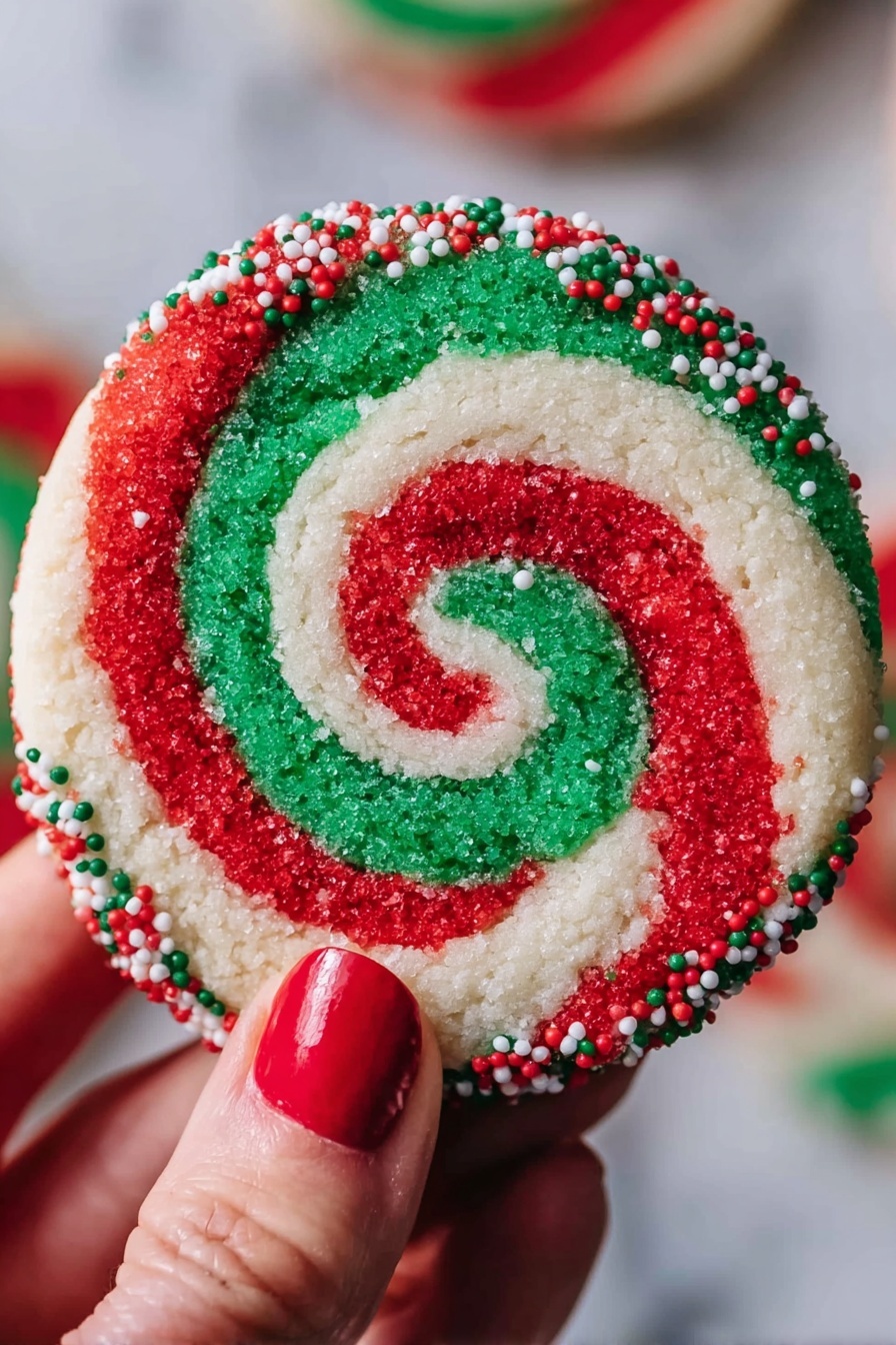A round cookie with a red, white, and green swirl pattern that forms a spiral from the center to the edges. The outer edge of the cookie is coated with small red, white, and green round sprinkles. A woman's hand with red nail polish holds the cookie against a blurred background, and the surface under the cookie is white marbled texture. photo taken with an iphone --ar 2:3 --v 7 - Swirled Christmas Cookies, Christmas Cookie Recipes, Holiday Cookie Ideas, Festive Cookie Baking, Easy Holiday Cookies
