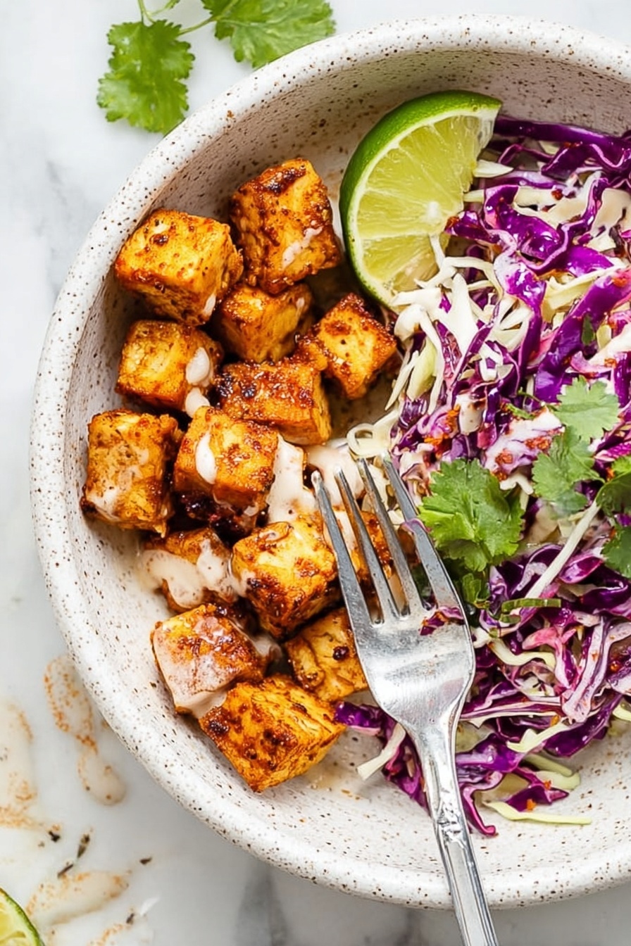 The image shows a white speckled bowl with two main layers: on one side, there are small, golden-brown seasoned cubes with a smooth light sauce drizzled over them, and on the other side, there is a mix of shredded purple and white cabbage with some green cilantro leaves scattered on top. A wedge of bright green lime sits at the edge of the bowl. A silver fork is placed inside, resting on the bowl’s edge and touching some of the cubes. The bowl is on a white marbled surface with some sauce drops visible nearby. Photo taken with an iphone --ar 2:3 --v 7 - Fish Taco Bowl with Spicy Mayo, Fish Taco Bowl, Spicy Mayo Fish Bowl, Quick Fish Taco Bowl, Healthy Fish Taco Bowl
