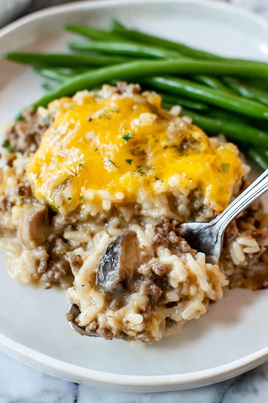 The dish shows two main layers on a white plate with green beans at the back. The bottom layer is a mix of cooked rice, ground meat, and slices of mushrooms, all combined in a creamy sauce with a light brown color and soft texture. The top layer is a covering of melted yellow cheese, unevenly spread, adding a slightly shiny and smooth look. The green beans are long and firm, bright green, placed behind the main dish. A silver fork is lifting a spoonful from the bottom layer, showing the mix of rice, meat, and mushrooms clearly. The plate is set on a white marbled surface photo taken with an iphone --ar 2:3 --v 7 - Cheesy Ground Beef and Rice Casserole, ground beef casserole, cheesy beef rice bake, easy beef casserole, comfort food recipes
