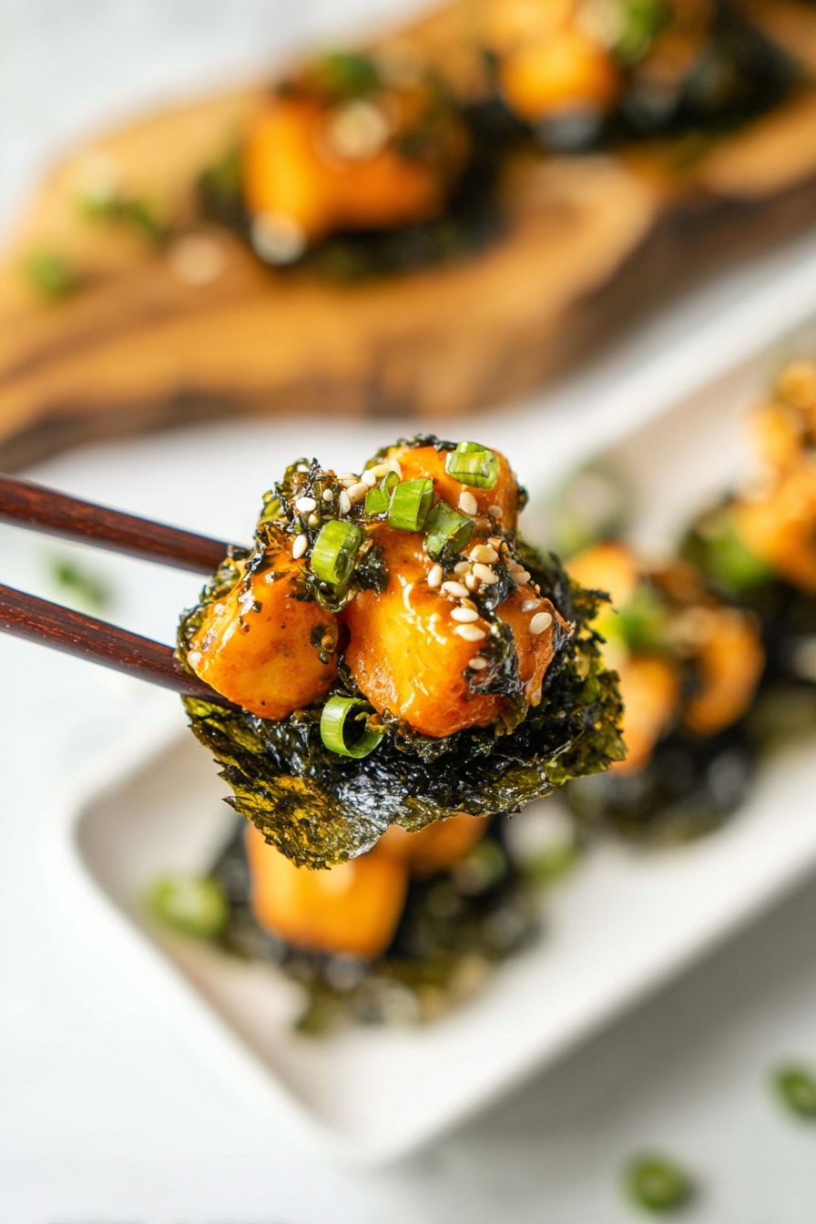A close-up of a pair of dark brown chopsticks holding a bite-sized stack. The bottom layer is a dark green, wrinkled seaweed sheet, crisp in texture. On top, there are several pieces of light orange cooked cubes with a glossy, slightly creamy bright orange sauce covering them. The stack is garnished with small white sesame seeds and chopped green onions that add green touches to the dish. In the background, a white plate with more similar stacks rests on a white marbled surface. A blurred wooden board with more stacks is visible behind the plate. Photo taken with an iphone --ar 2:3 --v 7 - Baked Salmon Sushi Cups, sushi cups with salmon, easy baked sushi bites, salmon sushi appetizer, no-roll sushi recipes